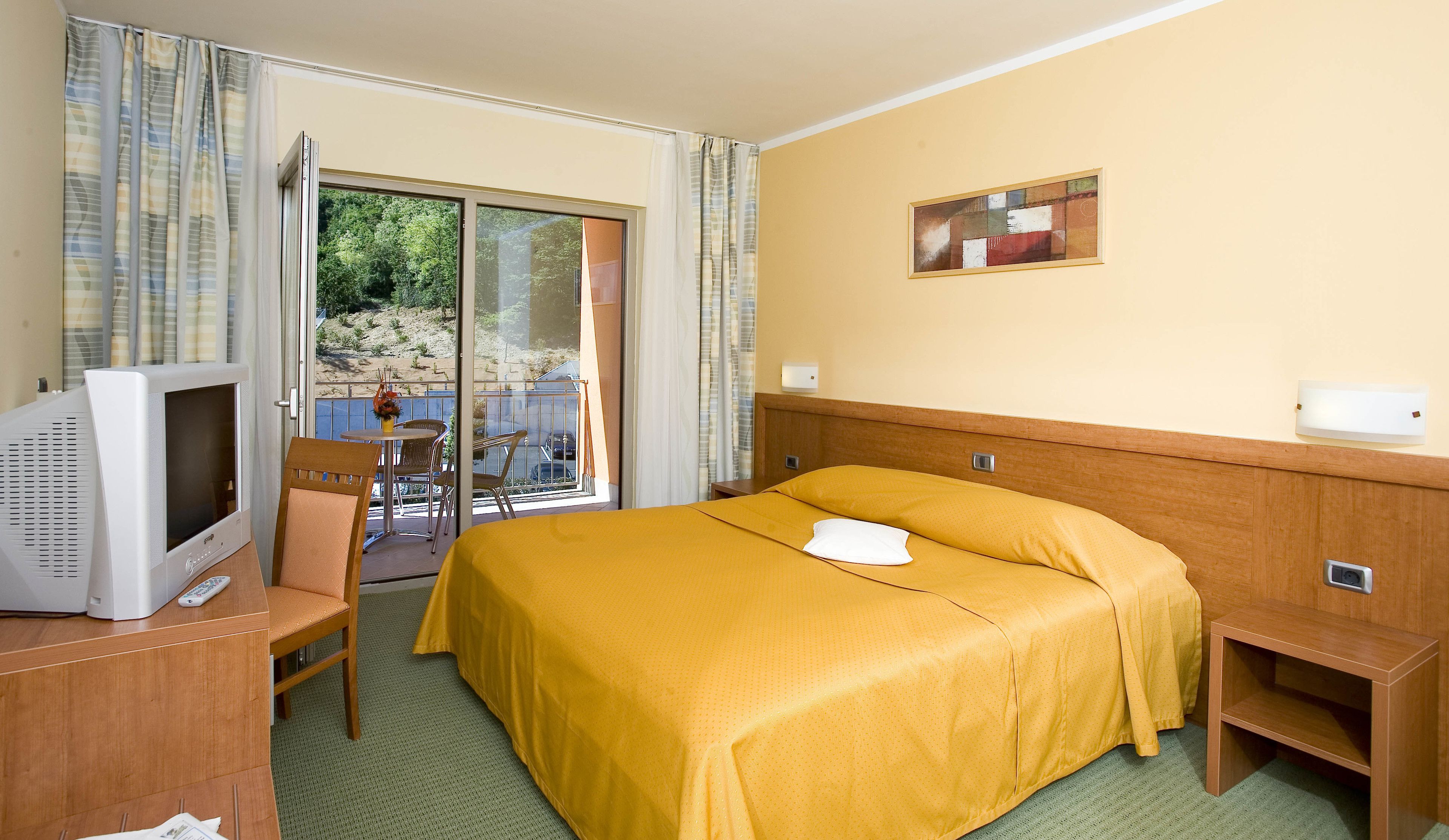 Una habitación de hotel con una cama, televisión, una mesita y una silla.