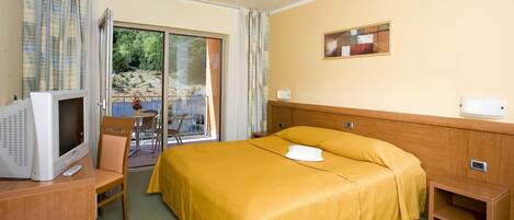 Una habitación de hotel con una cama, televisión, una mesita y una silla.