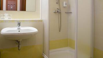A bathroom with a white sink, a glass-enclosed shower, and yellow-tiled walls.