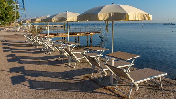 A beachside area with rows of sun loungers and umbrellas, a pier extending into the water, and a clear sky. - Hotel Salinera - Sava Hotels & Resorts (Piran)