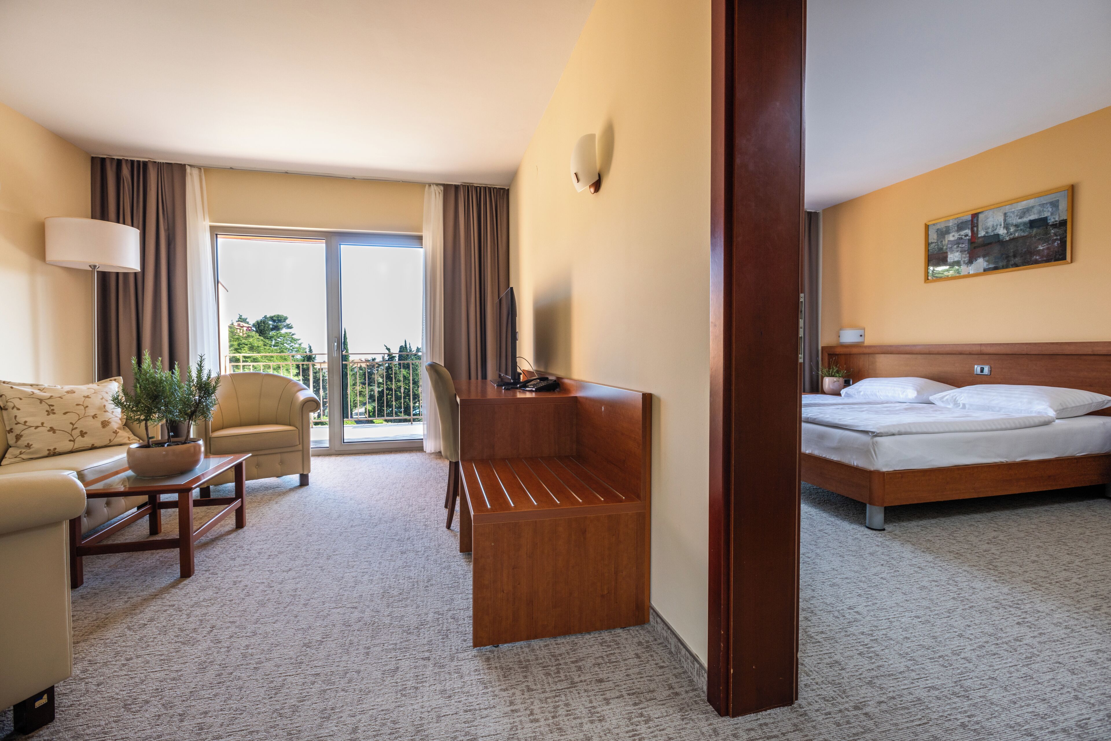A hotel room with a bed, a sofa, a desk, a chair, and a balcony with curtains.