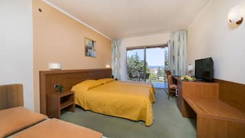 Una habitación de hotel con una cama, un escritorio con televisor, una silla, una mesita y un ventanal con vistas a árboles y edificios.