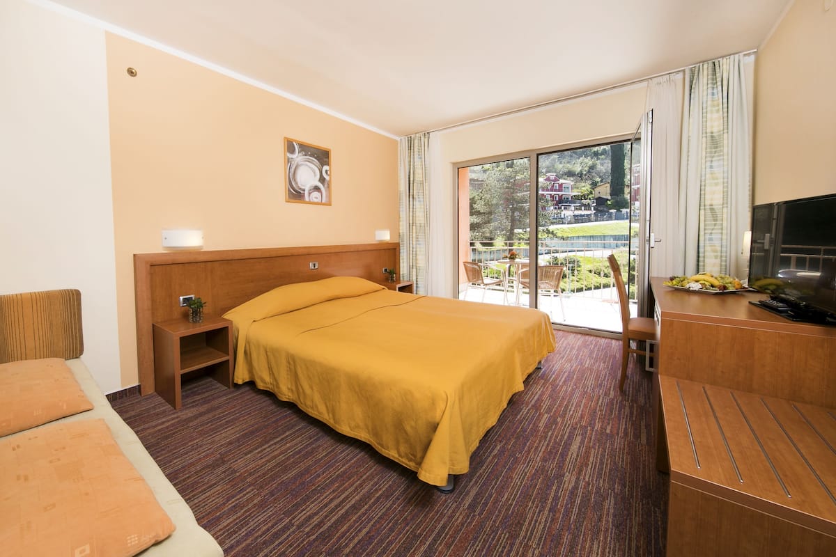 A hotel room with a bed, a desk with a TV, a balcony with a view, and a sofa.