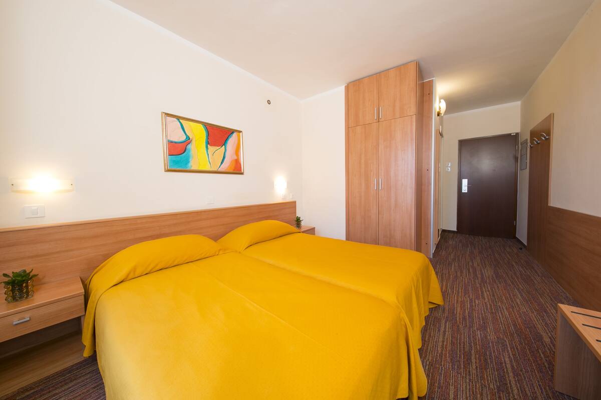 A hotel room with a large bed, wooden headboard, a painting on the wall, and a wooden wardrobe.