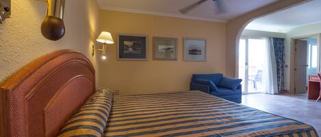 Habitación de hotel con cama, ventilador de techo, escritorio y vistas al exterior.