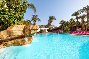 Una piscina con agua azul cristalina, rodeada de palmeras y una gran formación rocosa.