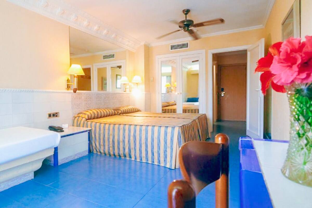 A hotel room with a large bed, a sitting area, a bathtub, and a ceiling fan.