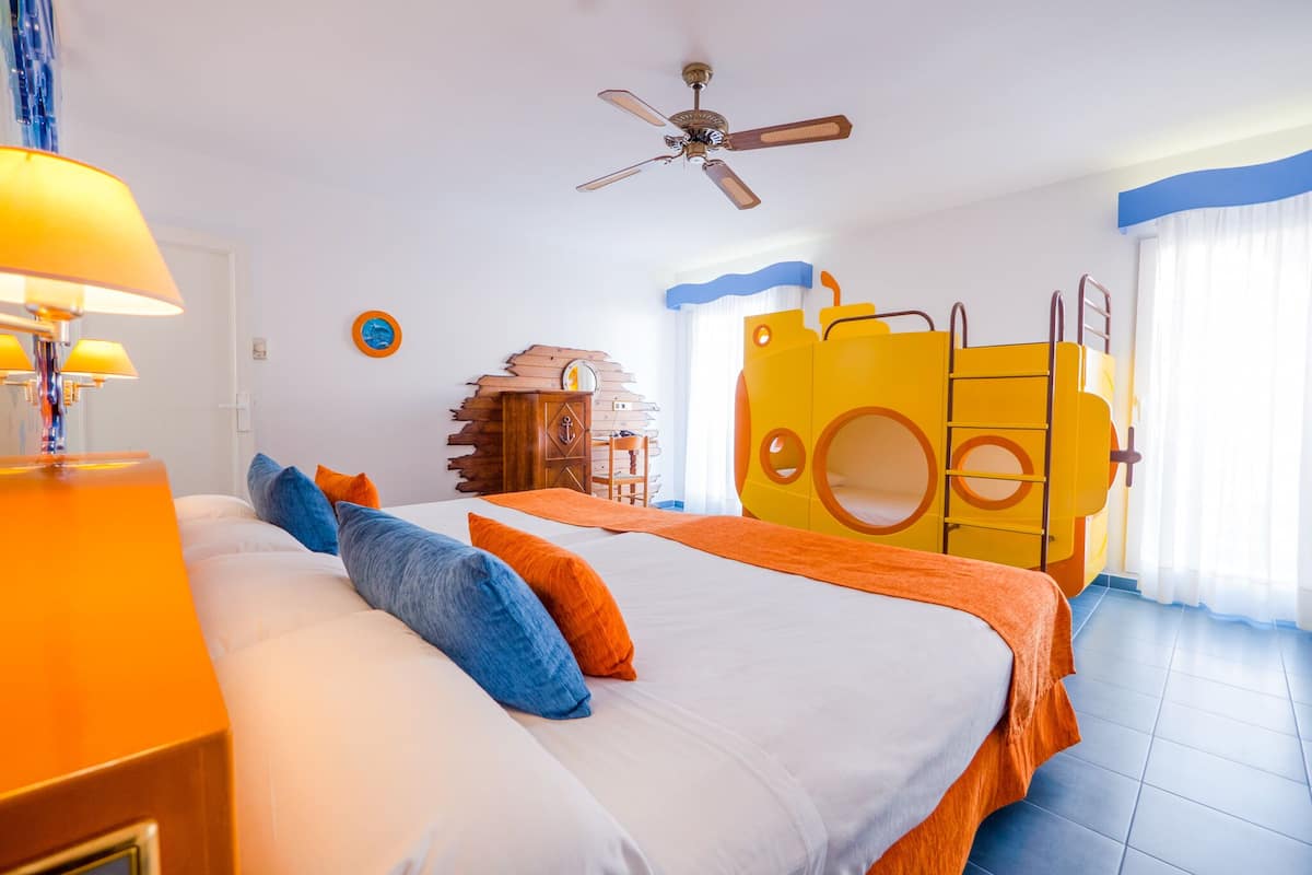 A hotel room with a bunk bed, a ceiling fan, a wooden cabinet, and a play area with a yellow structure.