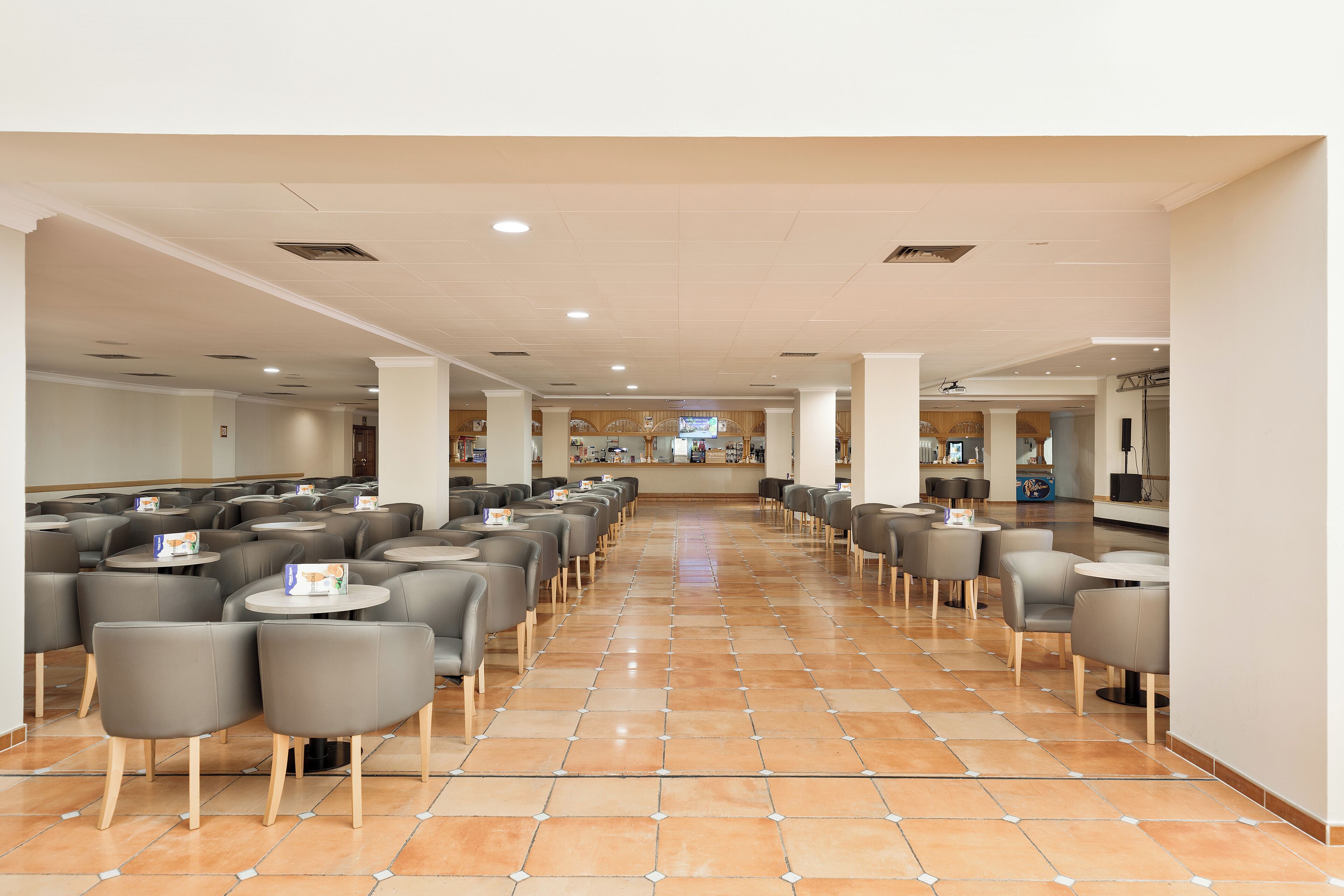 A spacious indoor area with rows of tables and chairs, a tiled floor, and a central walkway.
