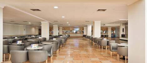 A spacious indoor area with rows of tables and chairs, a tiled floor, and a central walkway.