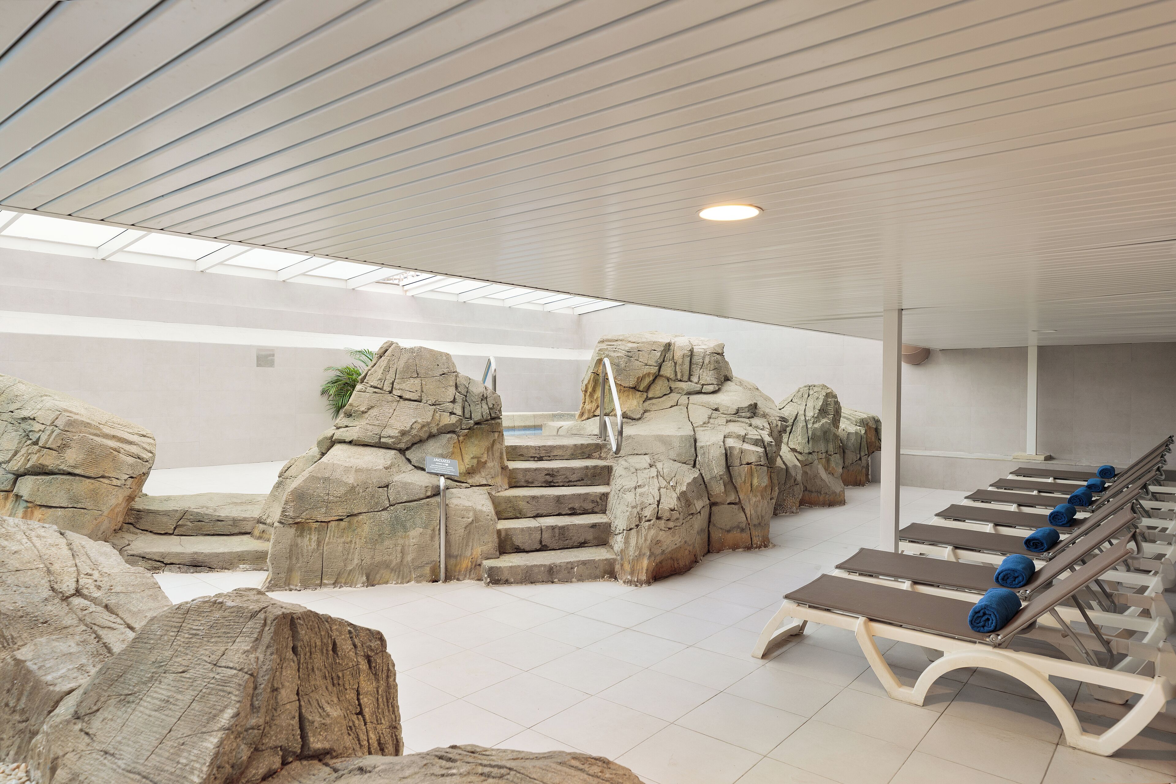 A spa area with a rock formation, a hot tub, and multiple sun loungers.