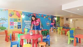 Un espacio interior luminoso con varias mesas y sillas, un mural en la pared y una persona al fondo.