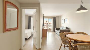 A hotel room with a bed, a dining table with chairs, a mirror, and a view of the outside.