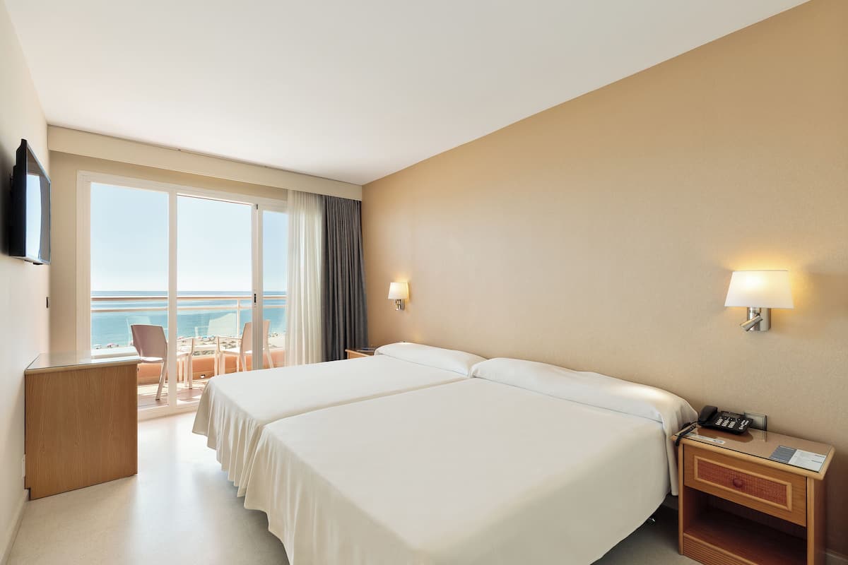 Habitación de hotel con dos camas, un escritorio, una silla, una mesita de noche con teléfono y vista al océano.