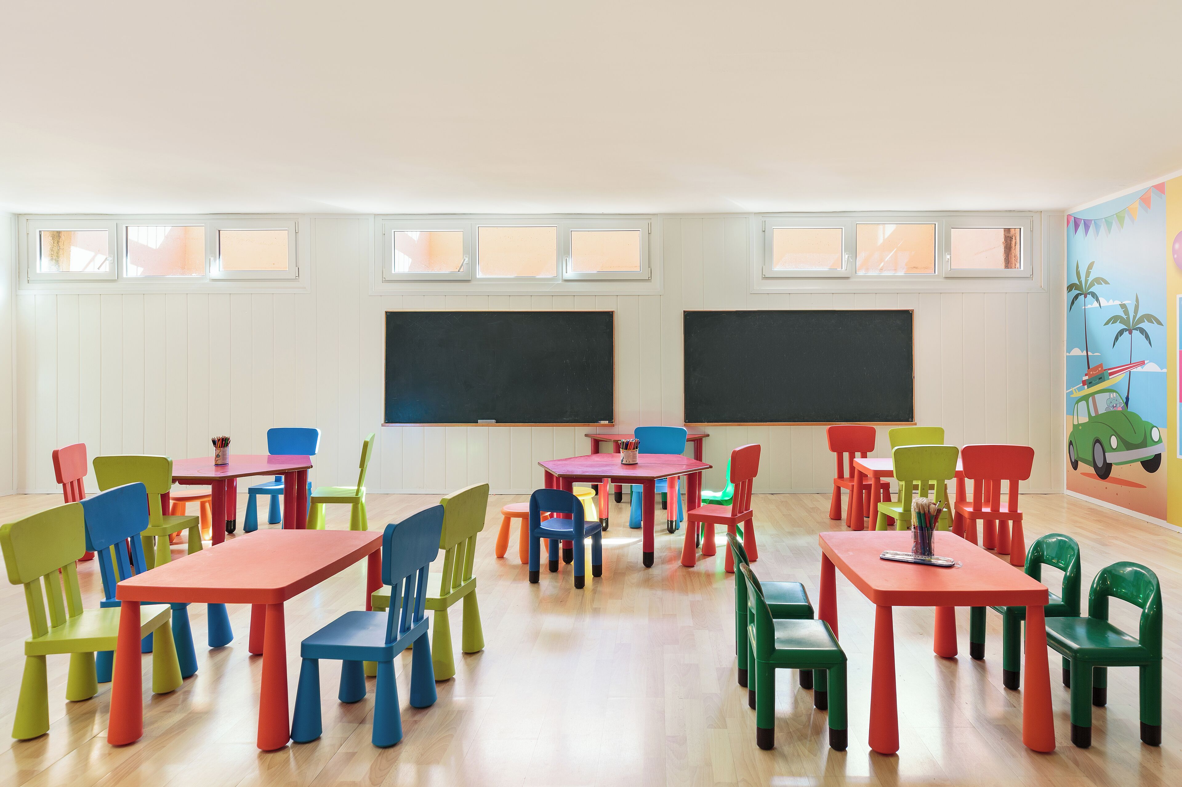 A classroom with colorful chairs and tables, white walls, and two blackboards.