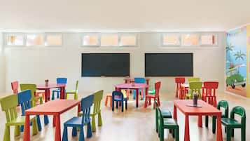 Un aula con sillas y mesas coloridas, paredes blancas y dos pizarras.