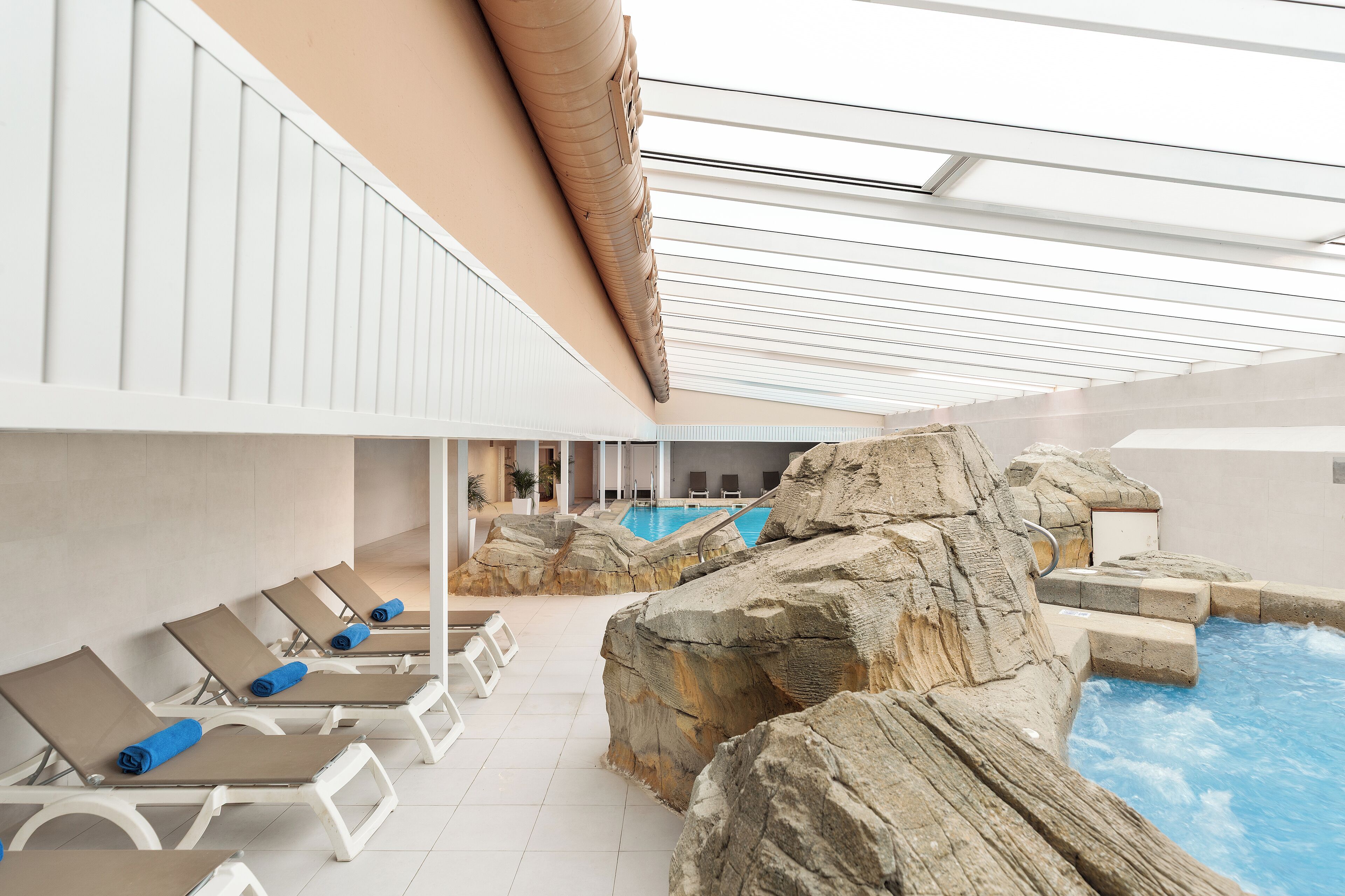 Un área de piscina interior con sillones de descanso y un paisaje rocoso de fondo.