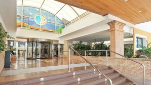 A spacious indoor area with a central staircase, a glass elevator, and a colorful mural on the ceiling.