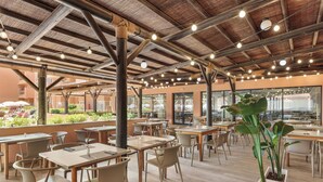 An outdoor cafe area with tables and chairs, a wooden ceiling, and potted plants.