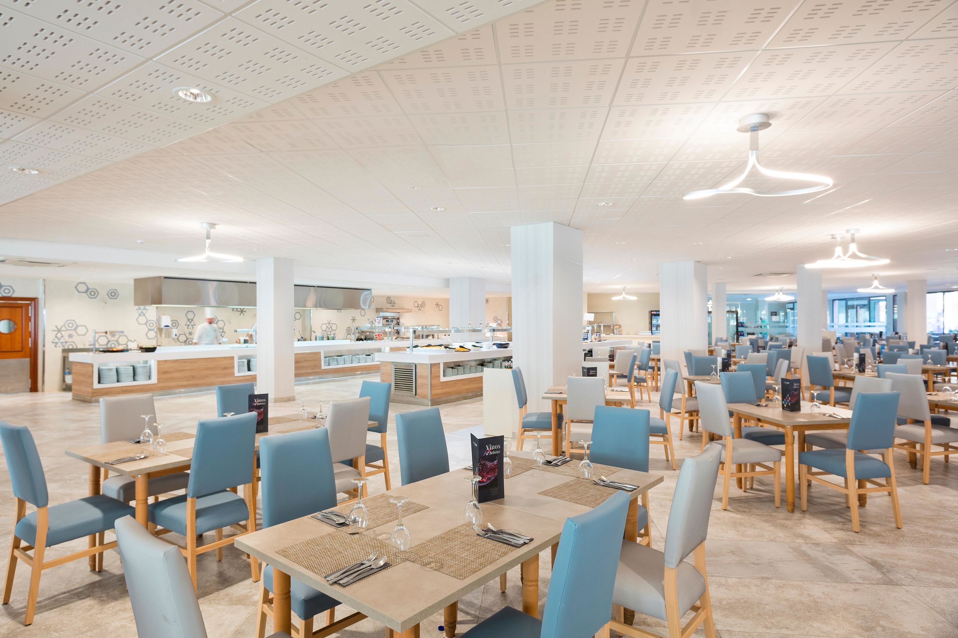 Un comedor amplio con varias mesas y sillas, una barra central y un diseño moderno de techo.