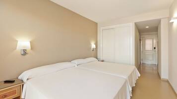Una habitación de hotel con dos camas, una mesita de noche, una lámpara y una puerta que da a otra habitación.