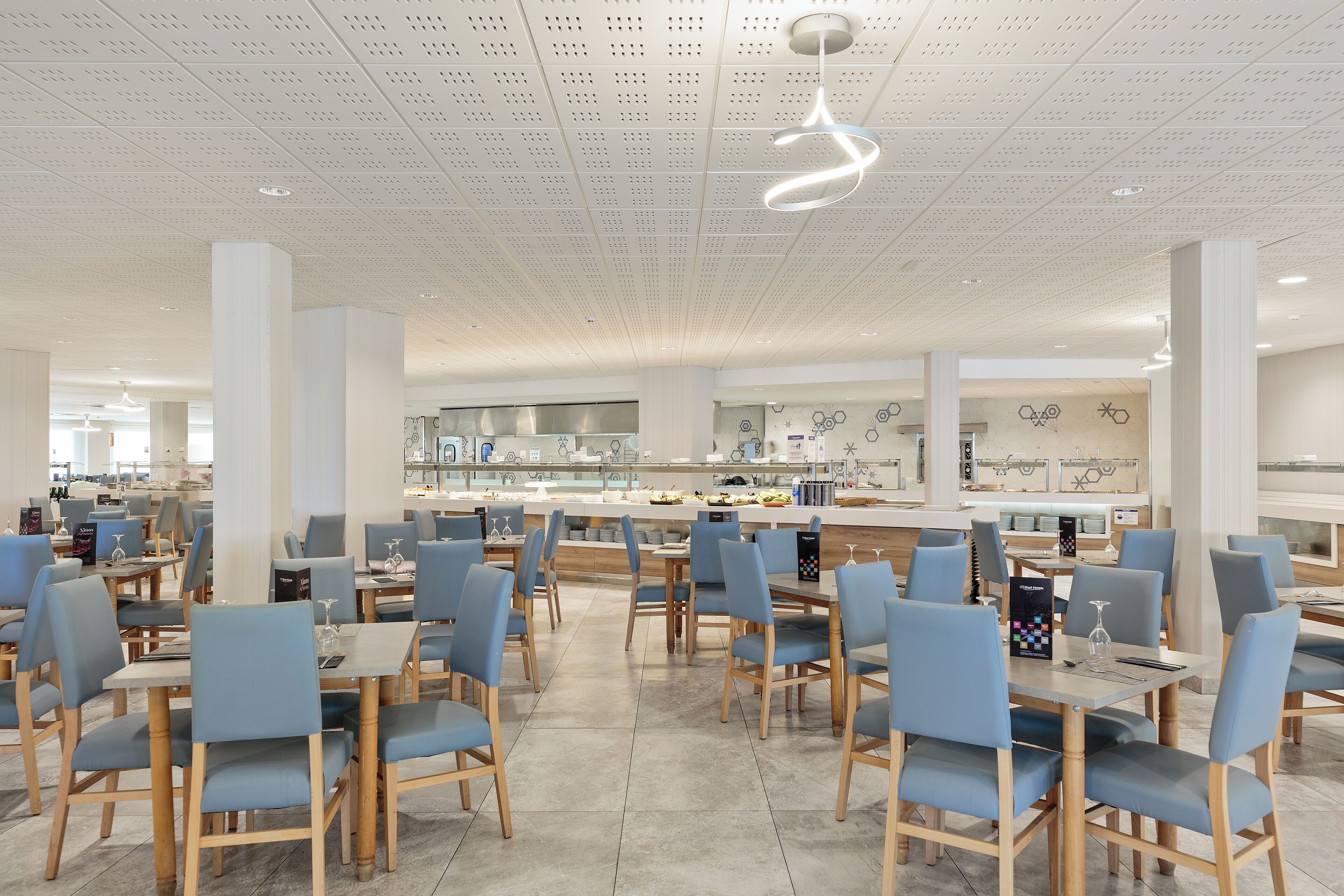 Un'area pranzo moderna con tavoli e sedie, un bancone centrale e un soffitto con un lampadario originale.