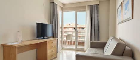 Una habitación de hotel moderna con un escritorio de madera, un televisor de pantalla plana, un sofá gris y un balcón con vistas a edificios.