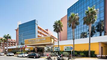 A hotel with a modern glass facade, palm trees, and a sign for Best Roquetas.