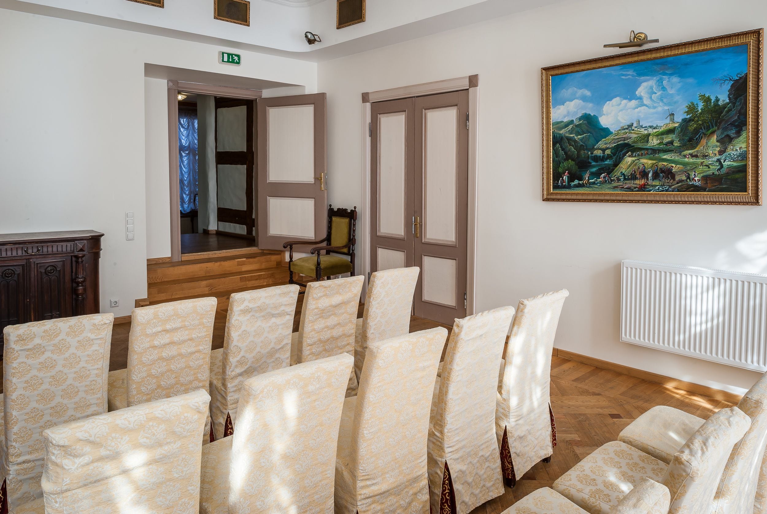 A conference room with rows of chairs, a painting on the wall, and a wooden staircase leading to another room.
