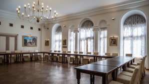 A large conference room with a long table and chairs, arched windows with curtains, and a chandelier. - St. Olav Hotel (Tallinn)