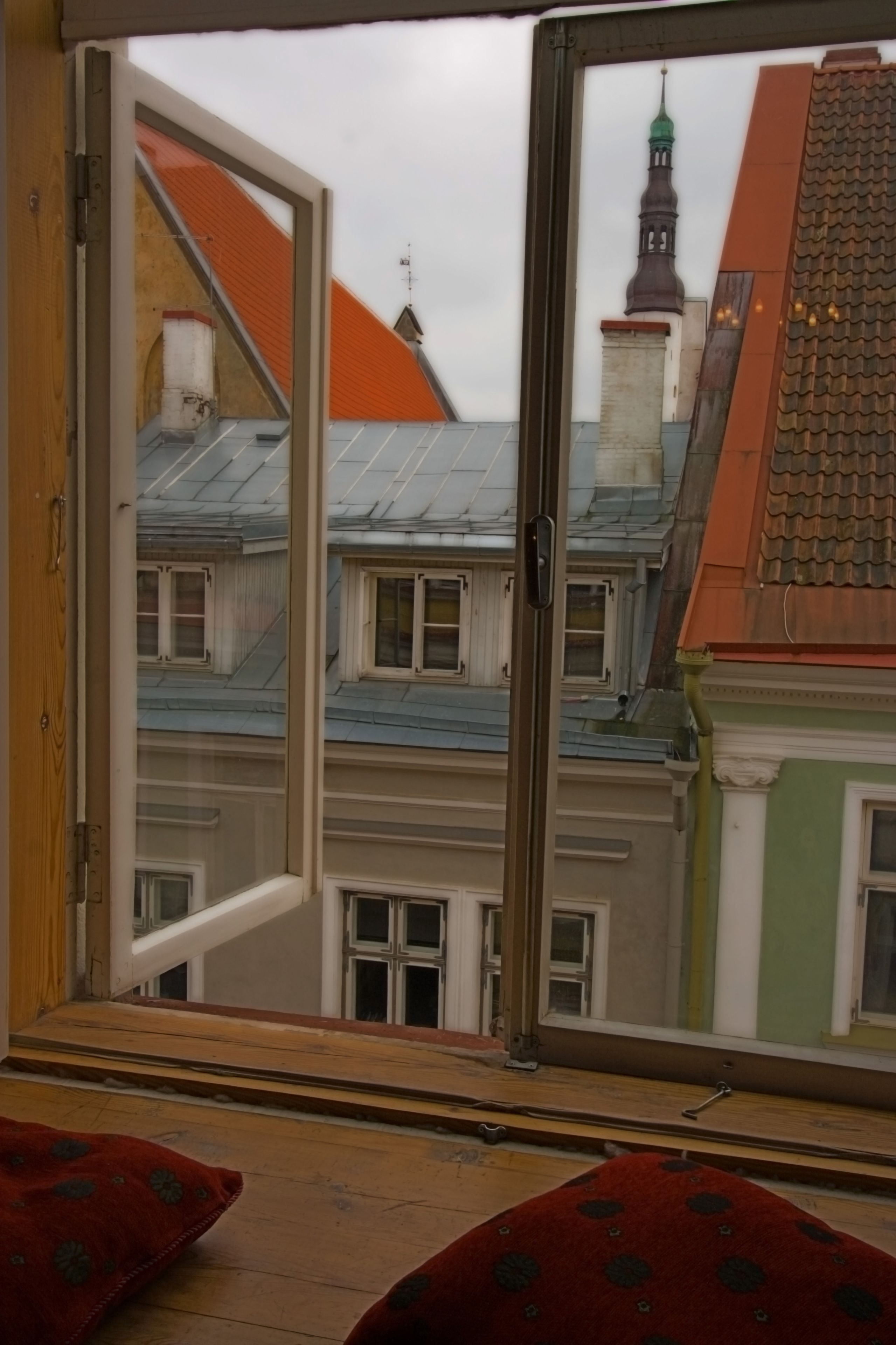 Ein Zimmer mit großem Fenster, Holzboden und roten, gemusterten Kissen.
