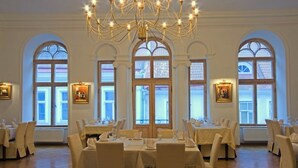 A dining area with tables set for service, large windows with arched tops, and a chandelier. - St. Olav Hotel (Tallinn)