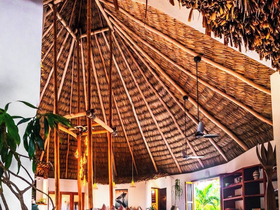 A spacious interior with a high thatched ceiling, a central seating area, and a view of greenery outside.