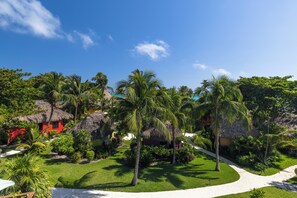 A tropical resort with thatched-roof huts, palm trees, and a well-maintained lawn.