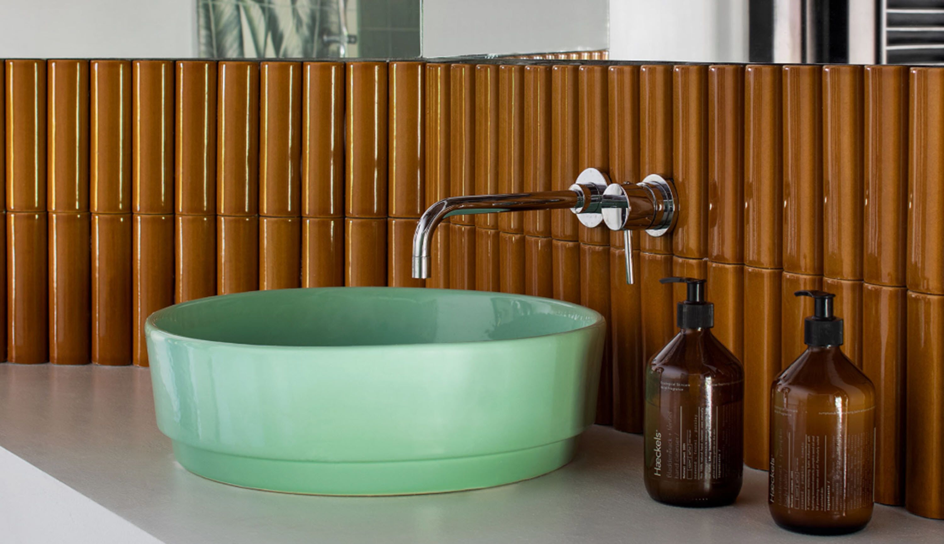 A bathroom with a green ceramic sink, a modern faucet, and two brown bottles of hand soap.