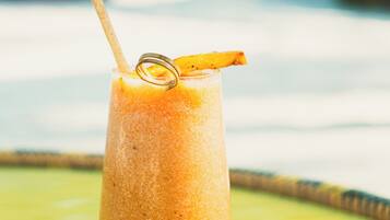 A tall glass of orange smoothie with a straw and a slice of orange on a white coaster, placed on a yellow table.