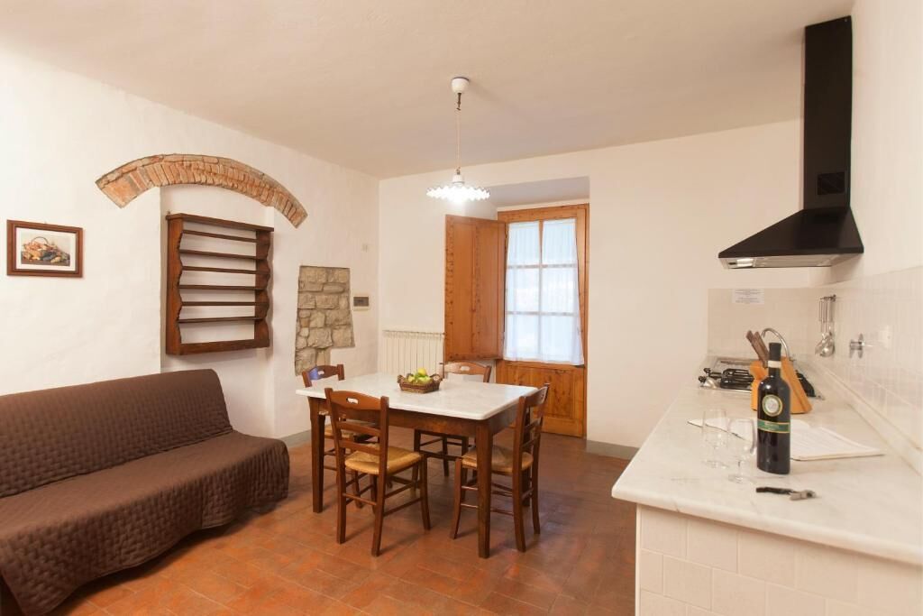 A kitchen with a dining table, chairs, a sofa, a stone archway, a wooden cabinet, and a black range hood.