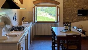 A kitchen with a gas stove, a window with a view, a stone wall, and a dining area with chairs.