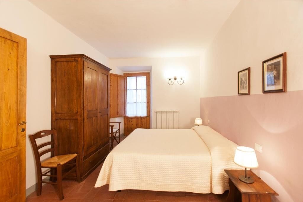 Une chambre à coucher comprenant un lit, une armoire en bois, une chaise et une table avec une lampe.