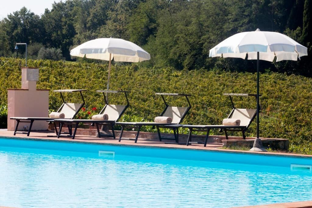 Una piscina con sillas de descanso y sombrillas, rodeada de vegetación.