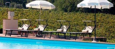 Una piscina con sillas de descanso y sombrillas, rodeada de vegetación.