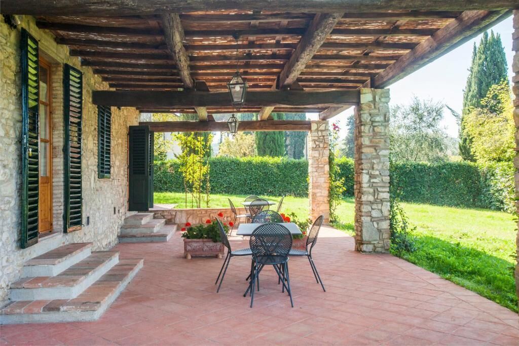 Eine überdachte Terrasse mit Steinstufen, einem Tisch und Stühlen und Blick auf einen Garten.