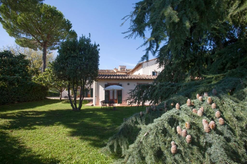 Una casa con techo de tejas, césped y un árbol con piñas.