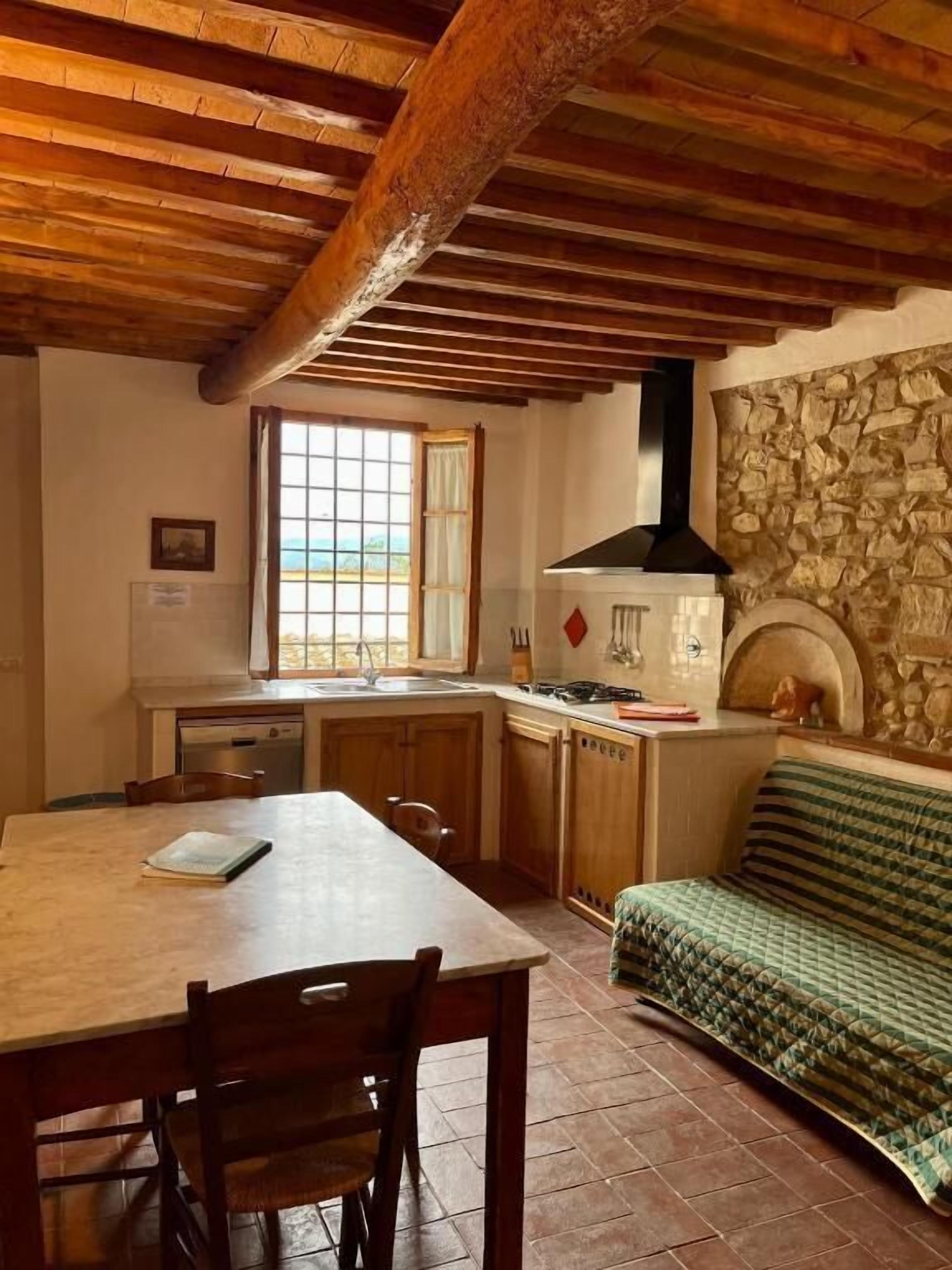 A rustic kitchen with wooden beams, a stone wall, a window, and a sofa.