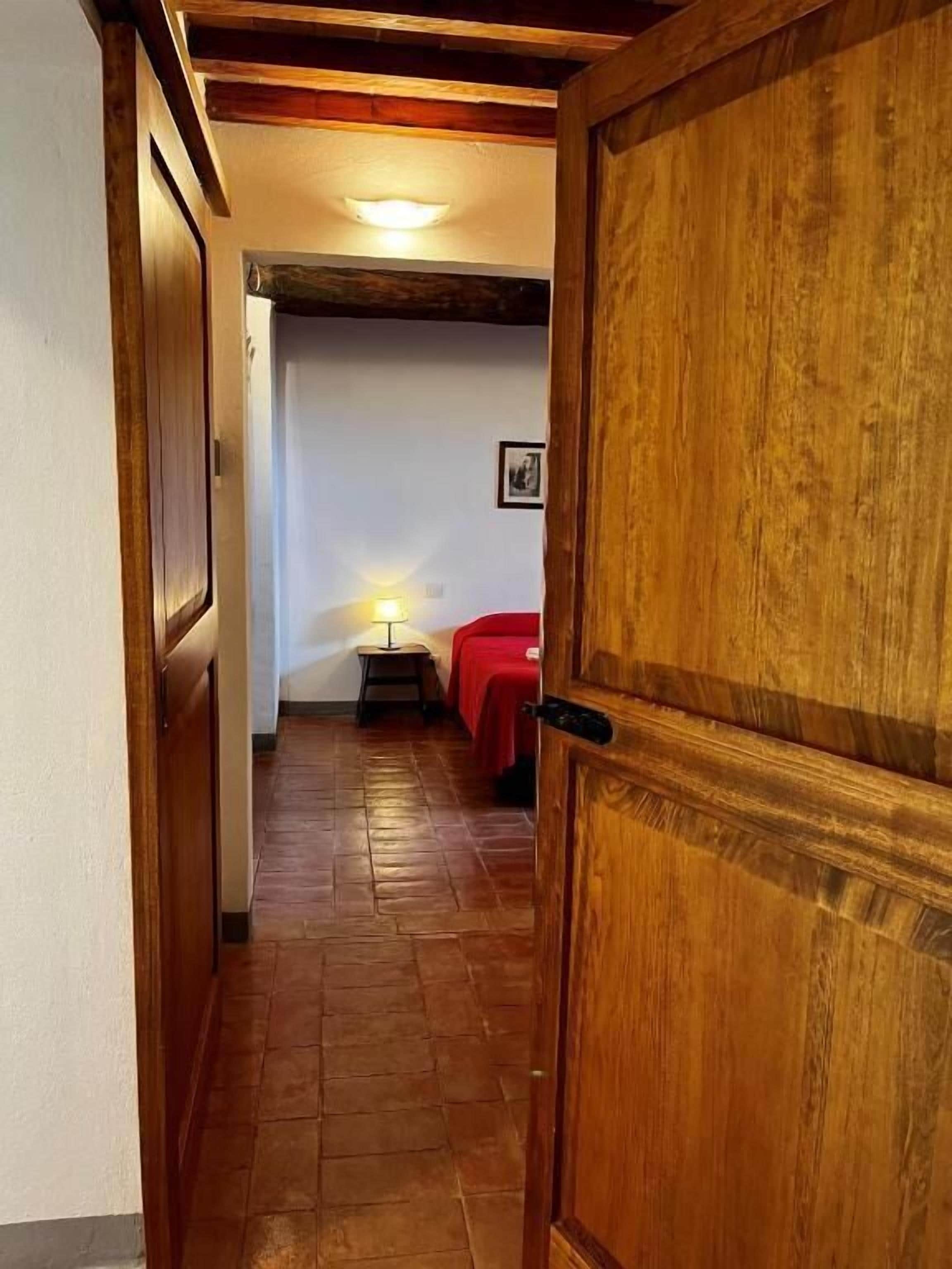 A hallway leading to a room with a bed, a nightstand, and a wall-mounted picture.