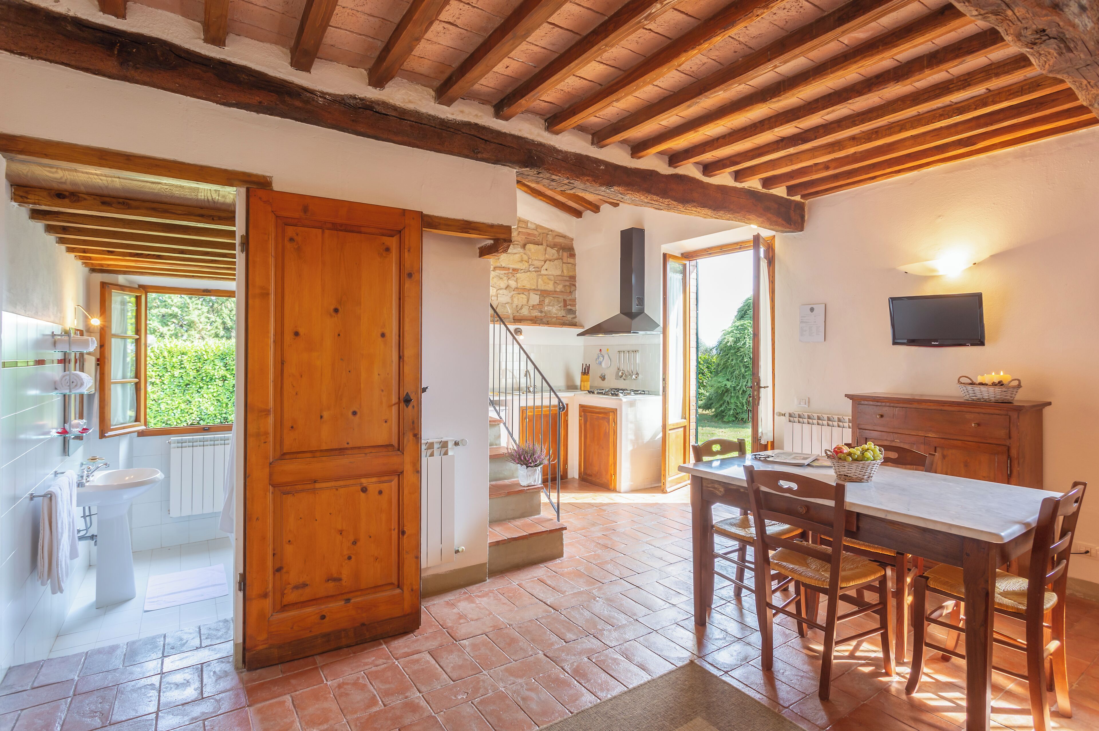 A rustic kitchen with a wooden door, a dining table with chairs, and a stone wall.