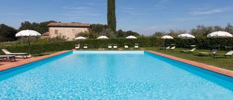 A rectangular swimming pool with clear blue water, surrounded by lounge chairs and umbrellas.