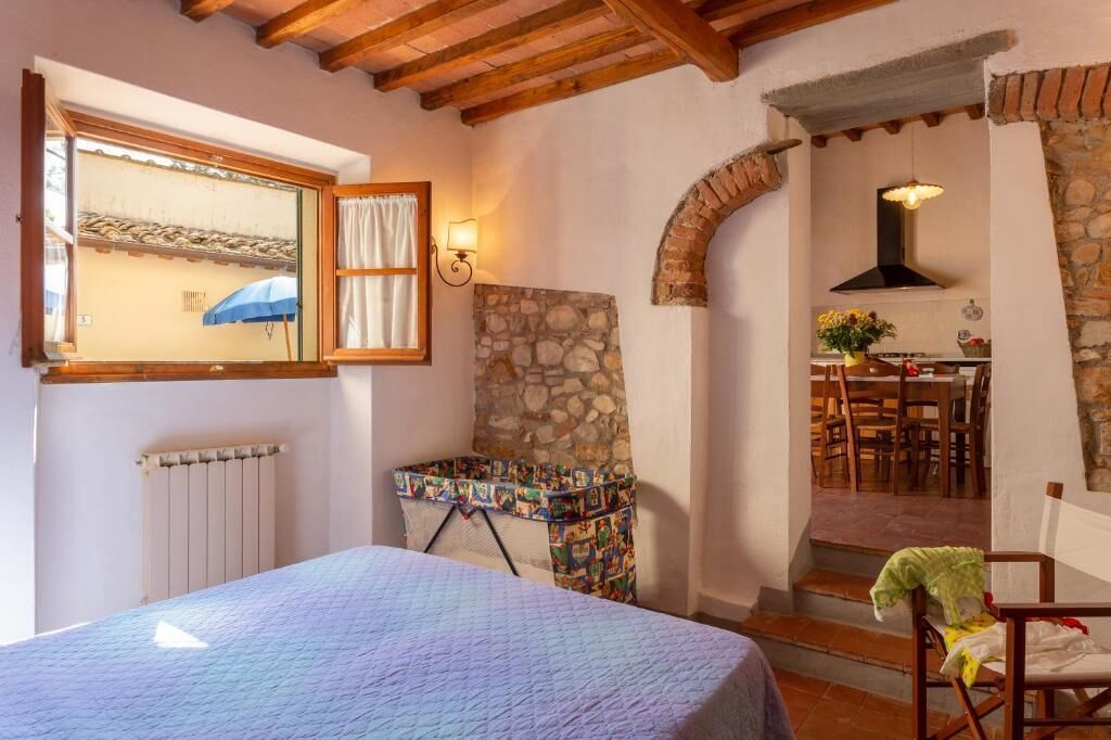 Une chambre à coucher avec un lit, une fenêtre avec des rideaux, un radiateur, un panier à linge et un mur en pierre.
