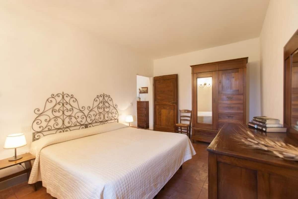 Ein Schlafzimmer mit einem Bett, einem Holzschrank, einem Schreibtisch mit Büchern und einem Stuhl.