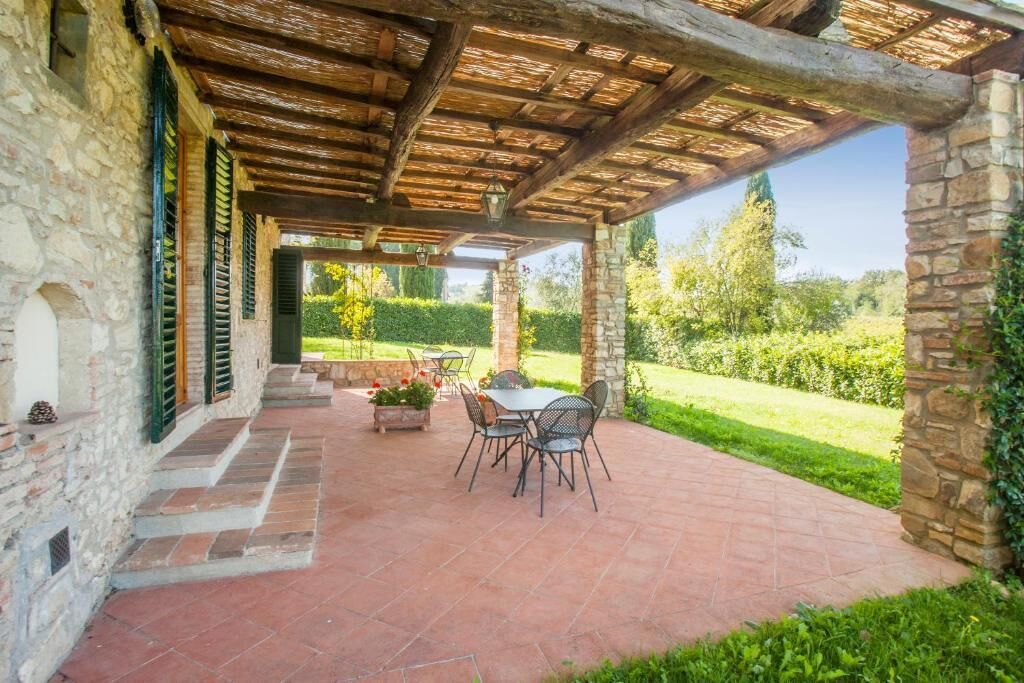 Une terrasse couverte avec des murs en pierre, une table avec des chaises et une vue sur un jardin bien entretenu.